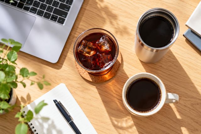 デスクに置かれたコーヒーカップ・グラス・ノートパソコンなどのイメージ
